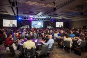 A large ballroom filled with people seated at round tables.