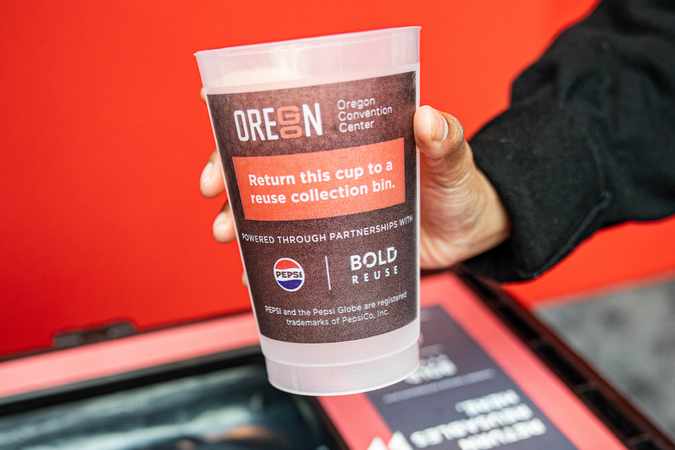 A hand holds a reusable cup with a black label.