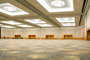 Spacious, empty ballroom hall with bright ceiling lights, beige walls, and patterned carpet. The room has a clean, modern, and neutral tone.
