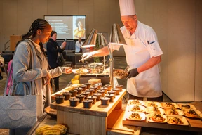 A chef prepares dishes under warm lights at a buffet.