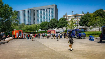 Food trucks in a plaza with a large hotel and trees.