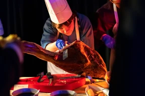 A chef carving a large steak on a red cutting board.