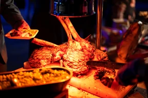 Grilled tomahawk steaks illuminated under warm light.