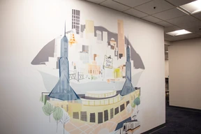 Abstract mural of a city skyline with stylized buildings, bridges, and trees on a white wall. The mural conveys a modern, urban vibe.