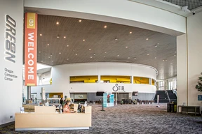 Spacious interior of Oregon Convention Center with a high ceiling, welcome banner, information desk, and modern seating area, conveying a welcoming tone.