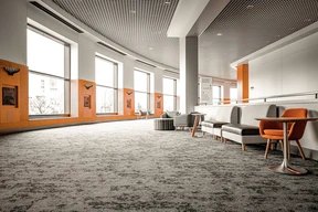 Modern lobby with large windows, gray carpet, and orange accents. Features gray and orange seating, creating a warm, inviting atmosphere.
