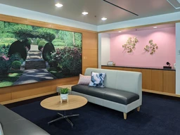 A cozy lounge with a gray sofa, floral pillows, and a wooden coffee table with a plant. A large garden mural and pink accent wall add warmth.